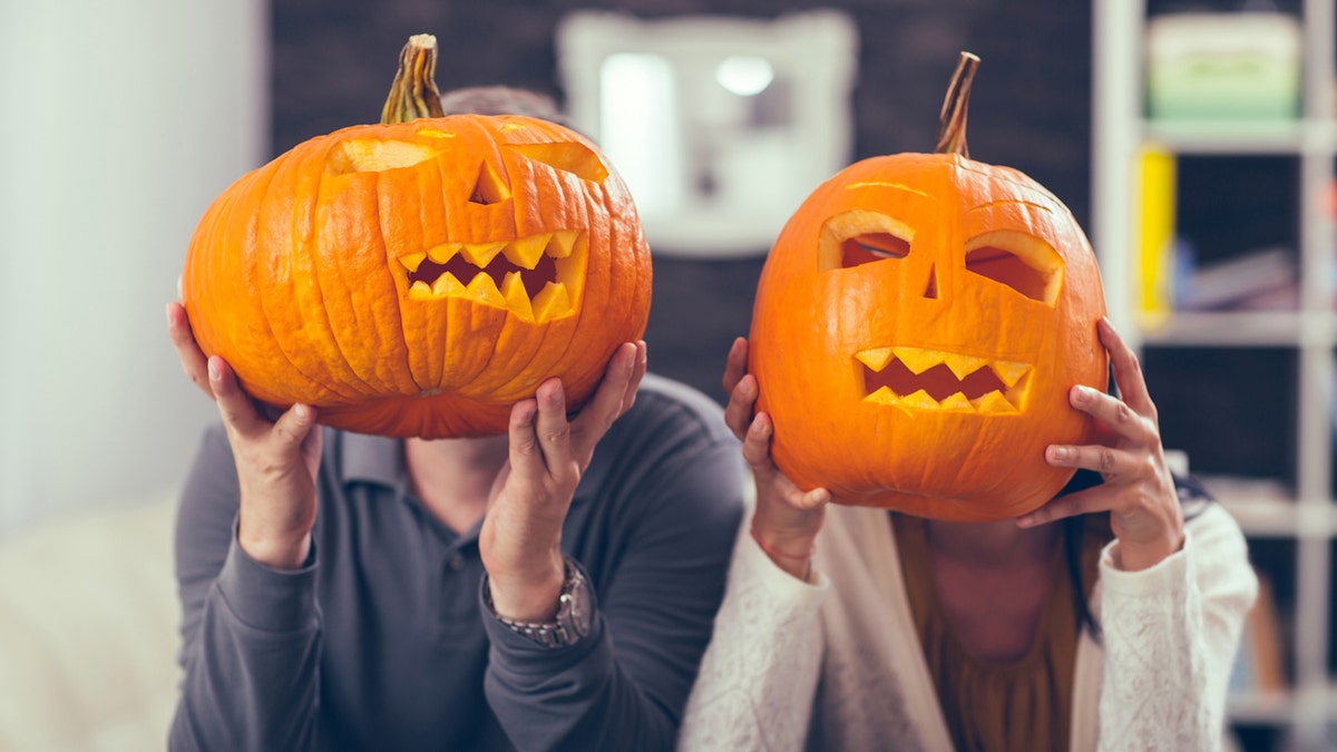 A man and woman hold carved pumpkins in front of their faces