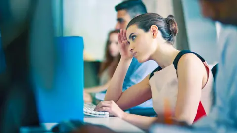 Getty Images Office worker sitting at her computer looking stressed.